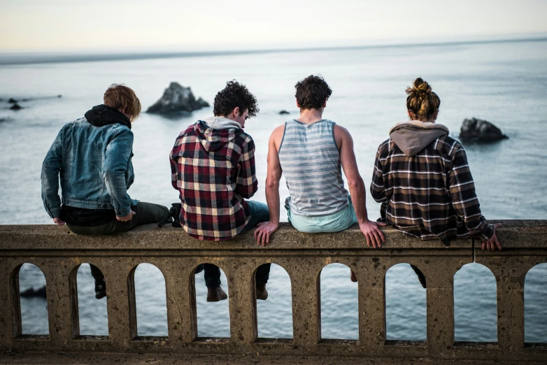 four people are sitting on a wall overlooking the ocean