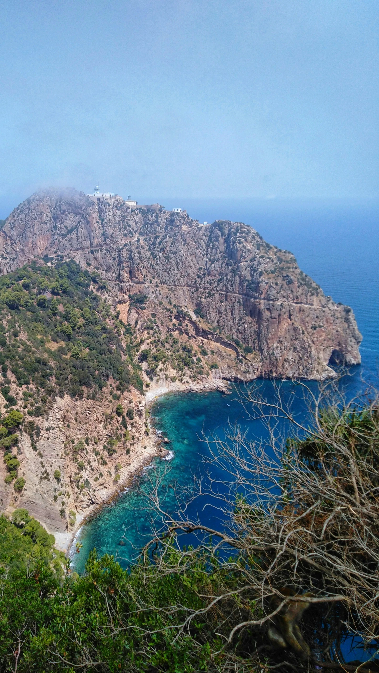 a mountain with trees on top and blue water