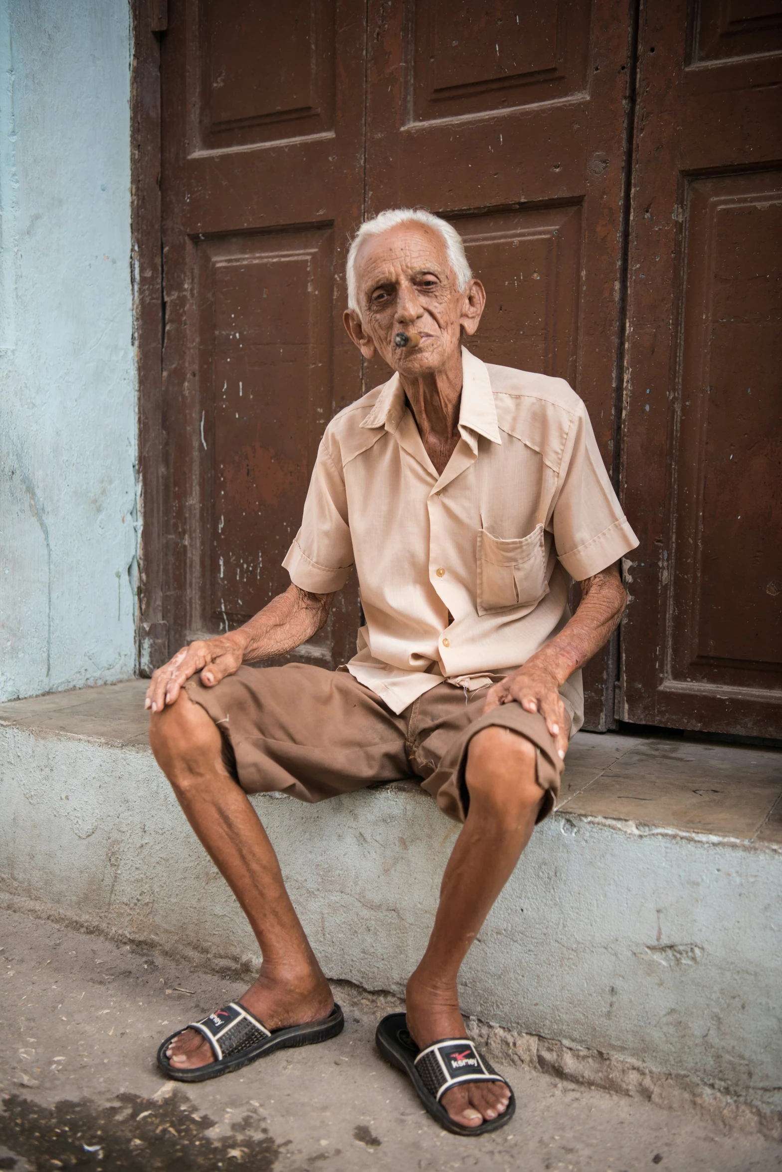 an older man sits outside his home by a wooden door