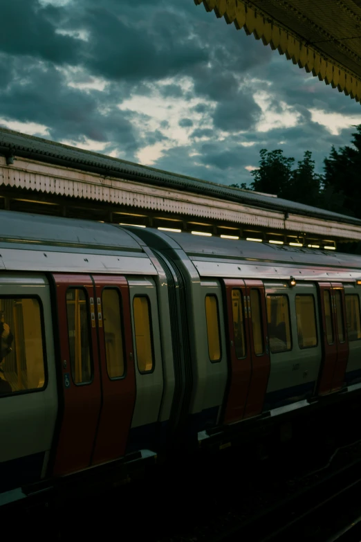 a long train sitting at the station under cloudy skies