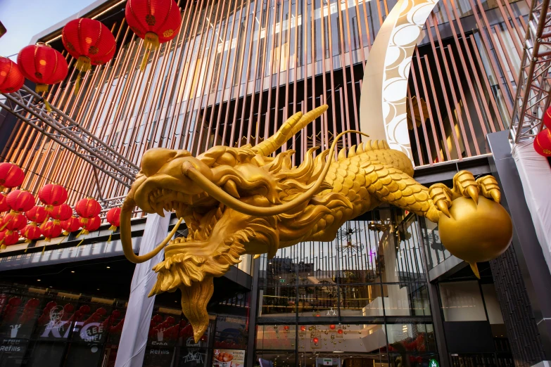 a gold statue sitting outside of a large building with red lanterns