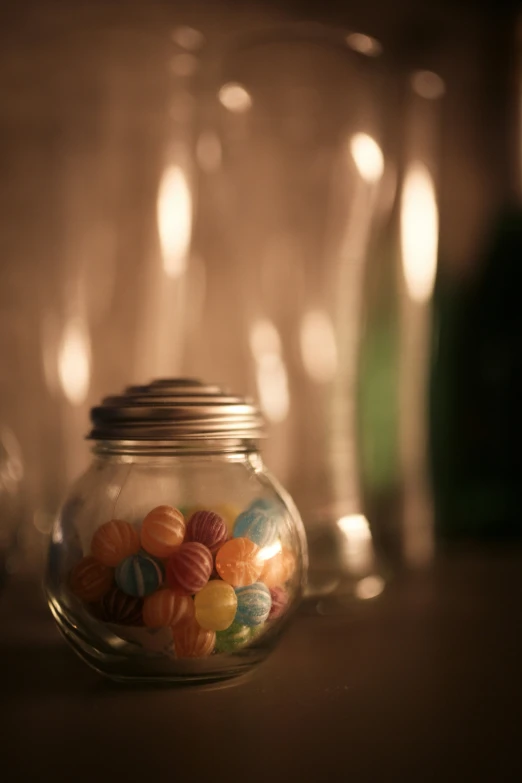 a glass jar with candy in it and some empty wine glasses behind it