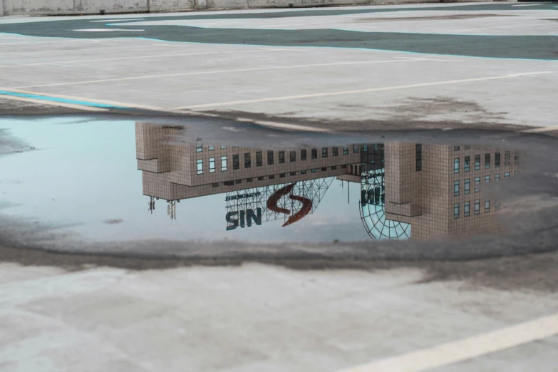 a reflection of a building in water next to an asphalt surface