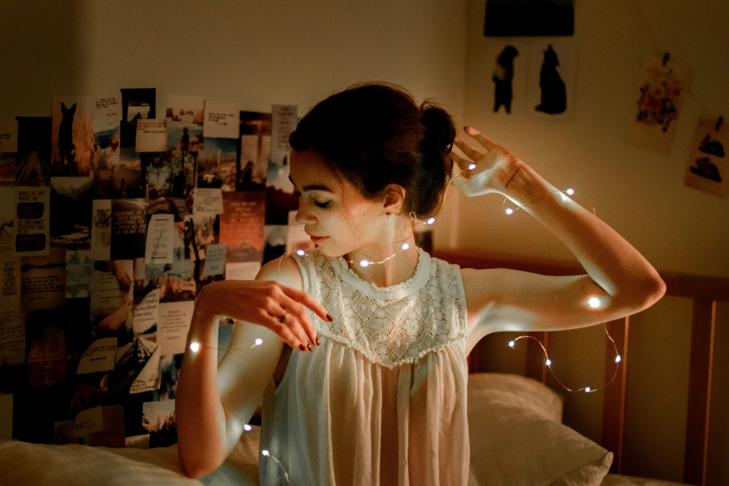 a woman standing by a bed wearing pajamas and stringing lights