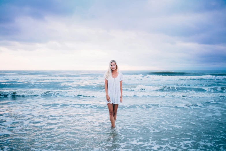 a beautiful young woman standing in the ocean on top of a surfboard