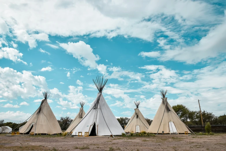 five teepees are standing on the field under a blue sky