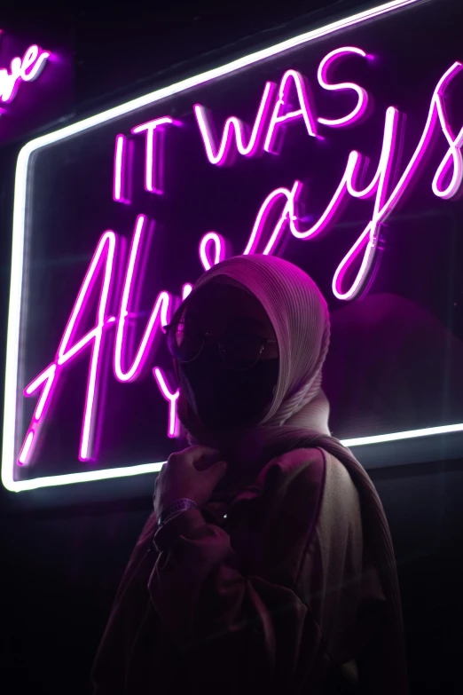 a man in a hoodie standing in front of a neon sign