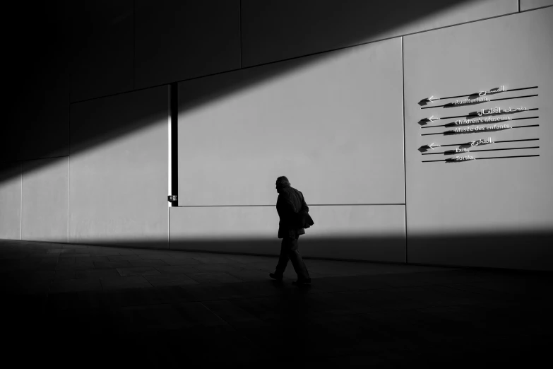 a man is walking past a building with long shadows