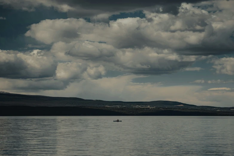 a man in a boat with dark clouds hovering over the land