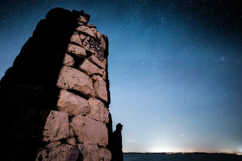 the man is standing on the rocks looking up at the stars