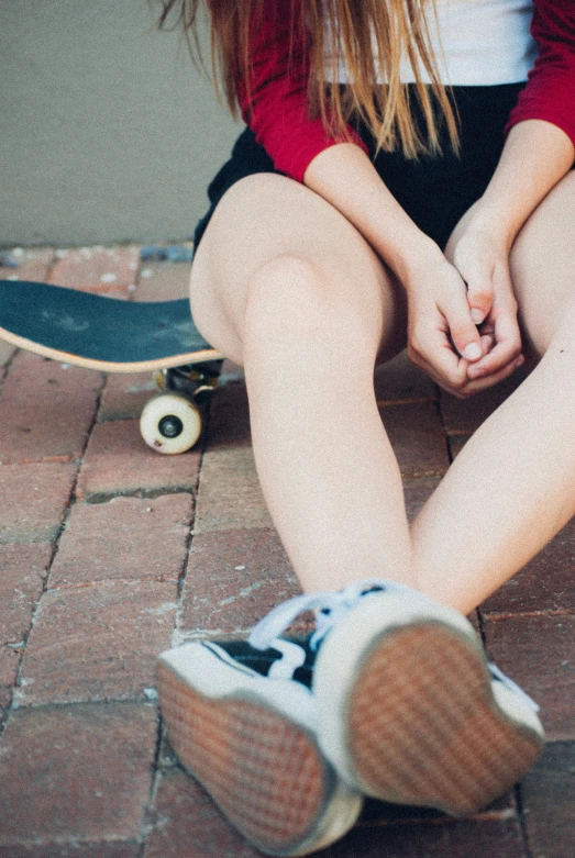 a girl wearing tennis shoes sitting on the ground with her feet crossed