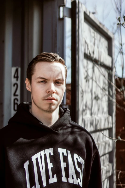 a young man wearing a black hoodie and standing next to a building