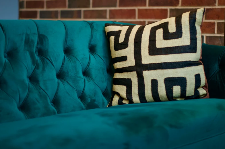 a blue velvet couch with an accent pillow on it