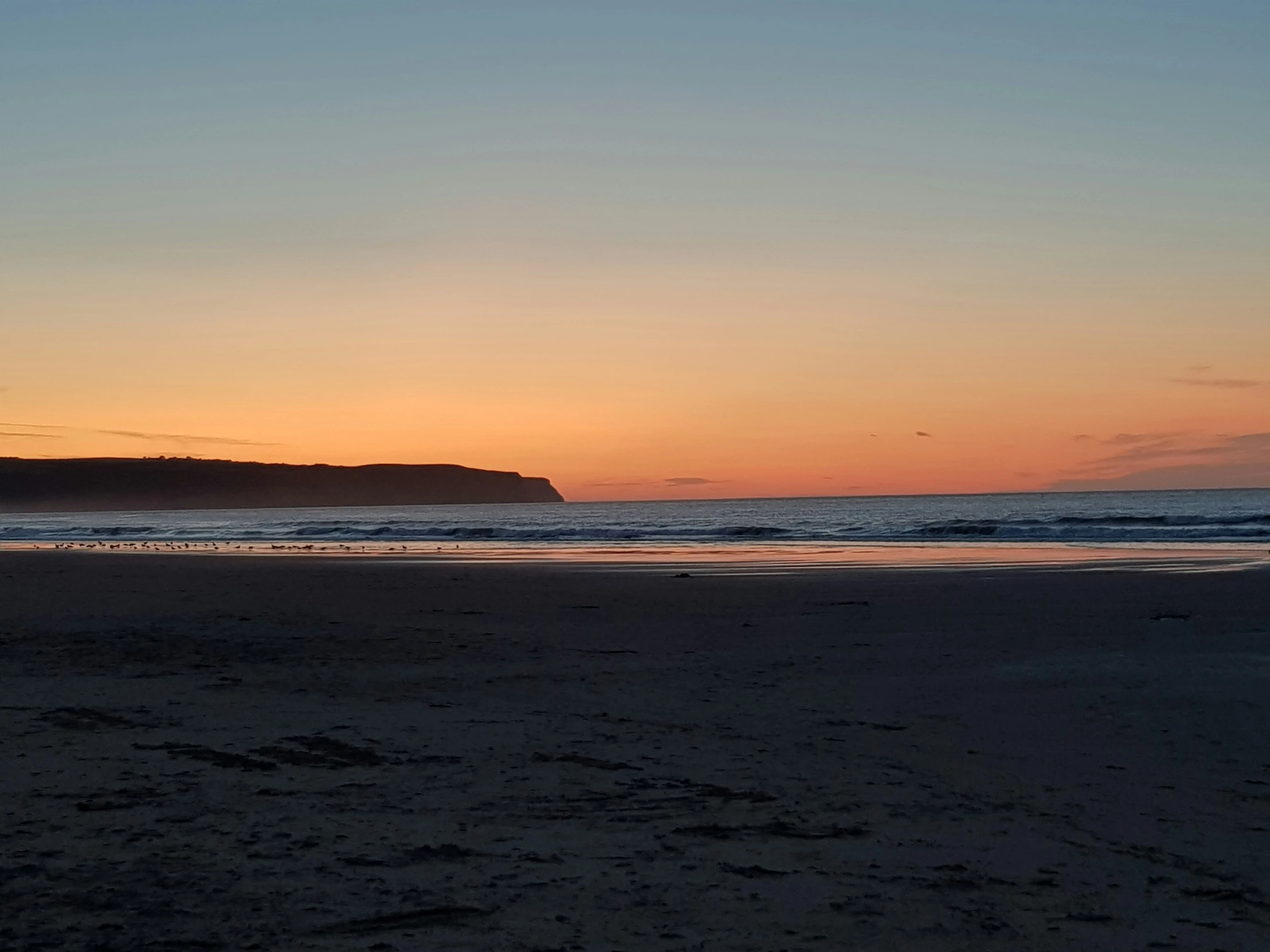 a lone surfer stands on the beach watching the sun set