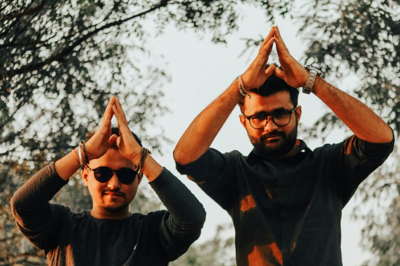 two men wearing sunglasses and a black top with trees in the background