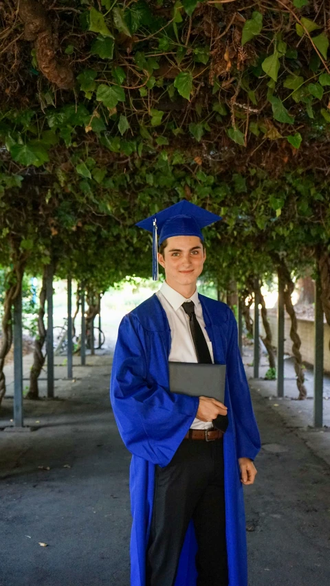 a male in a blue cap and gown is holding a folder