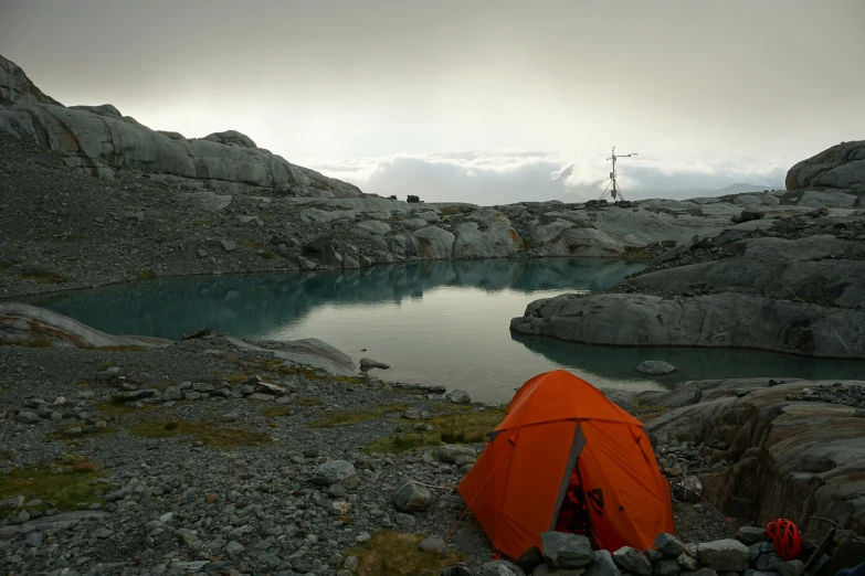 an orange tent sitting on a rock next to a pond