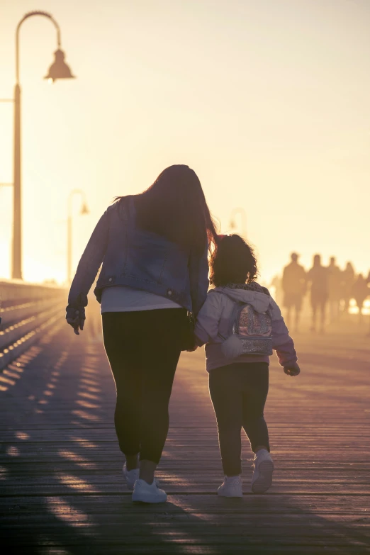 two woman in jeans walk with a little girl on the boardwalk