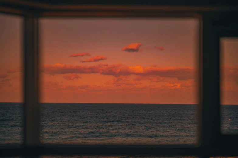 a view out of a window at an ocean at sunset