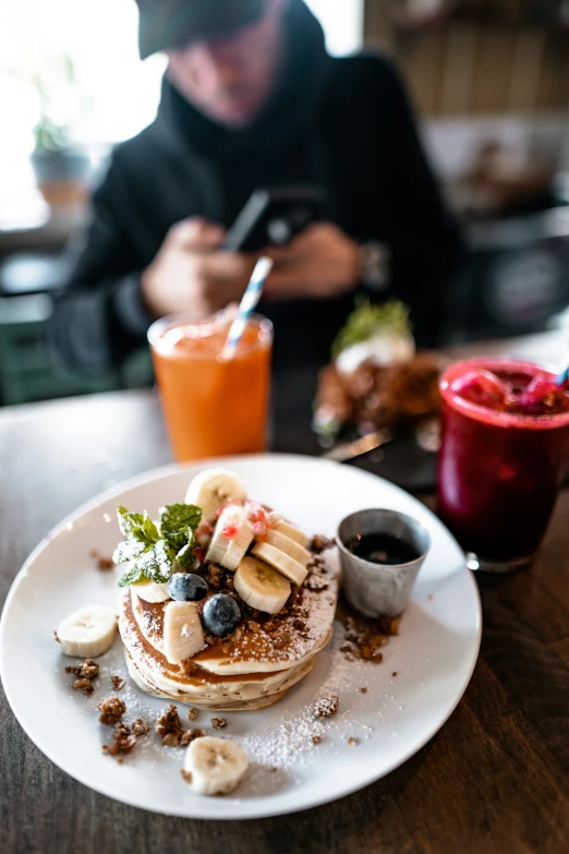 a man sitting at a table with some fruit and banana's on top of pancakes