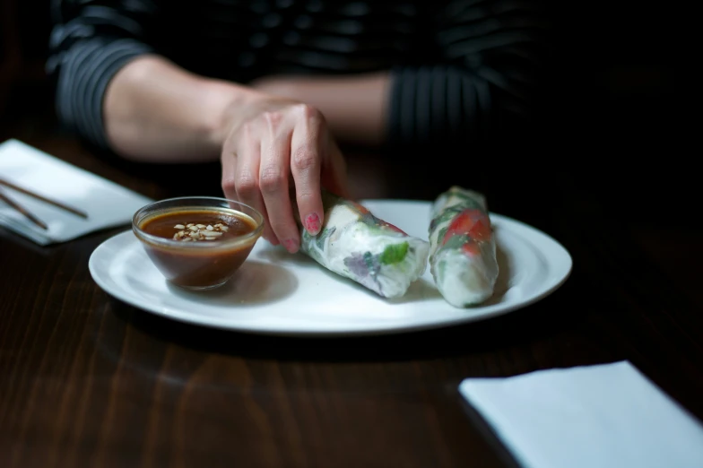 a plate with some dipping sauce and someone grabbing a sushi