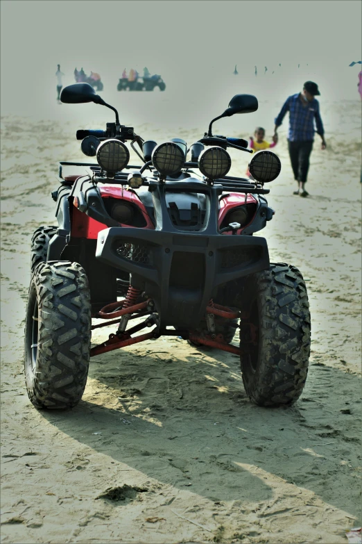 a four wheeler parked on the beach with people walking nearby