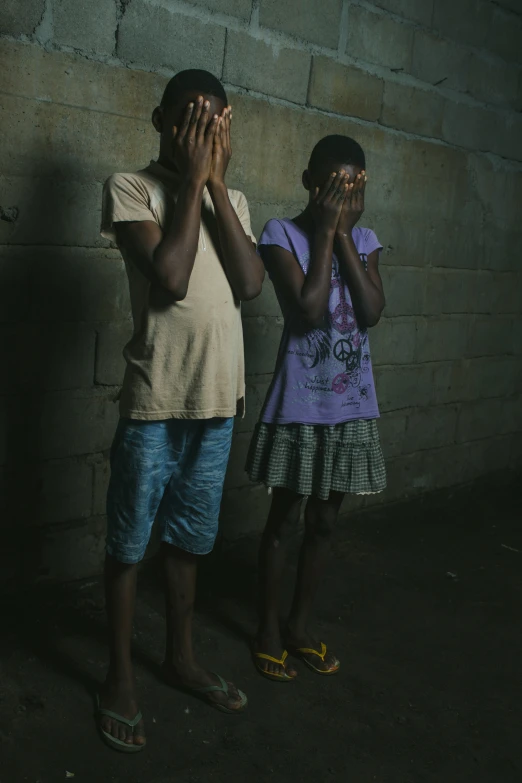 two children standing side by side in front of a brick wall