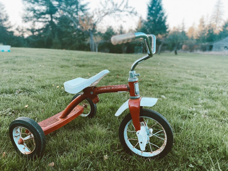 a red tricycle with a large metal tool resting on a grassy field