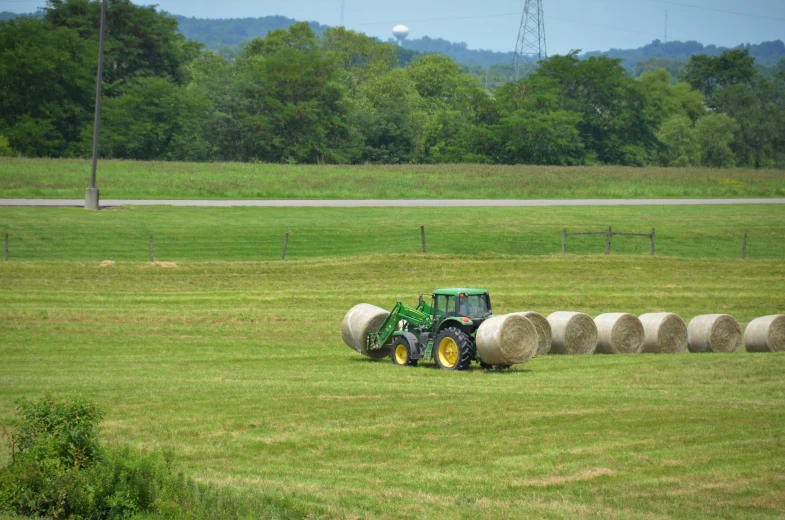 a green tractor plowing hay on a large open field