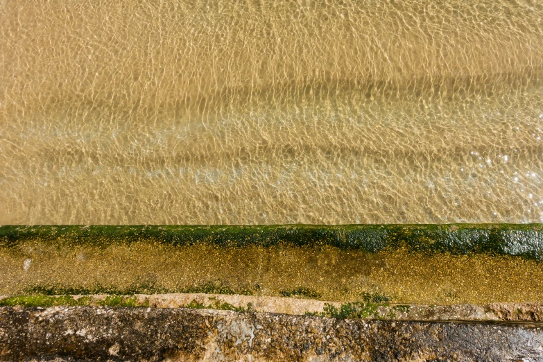 an aerial view of water, sand and a stone wall