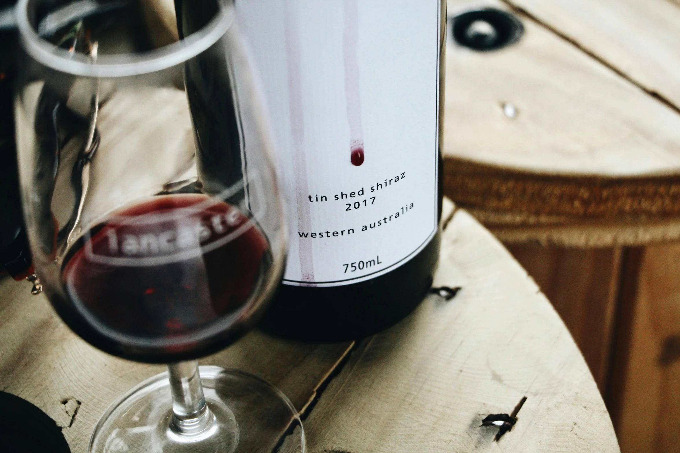 a glass of red wine sitting next to a bottle on a wooden table