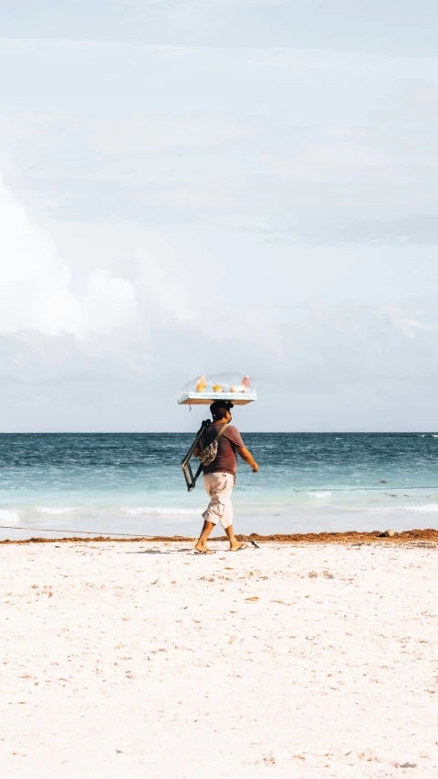 a man walking on a beach with a surfboard on top of his head