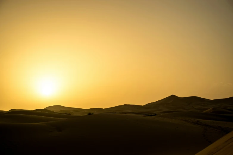 a desert scene with the sun setting in the distance