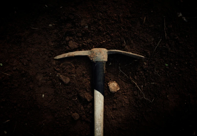 an axe stuck in the dirt near a shovel