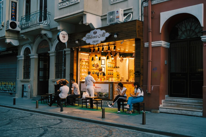 group of people sitting outside a store with lit windows