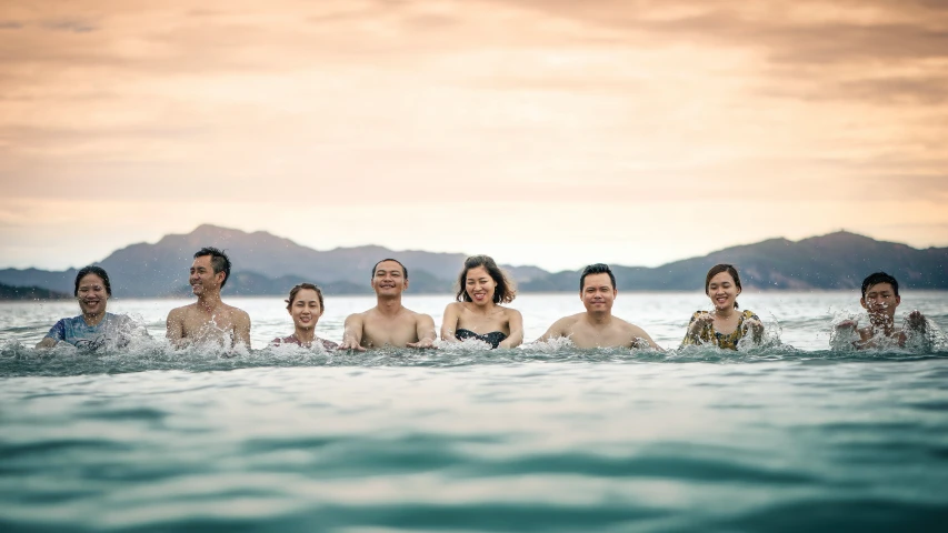 five people in the ocean swimming together with mountains in the background