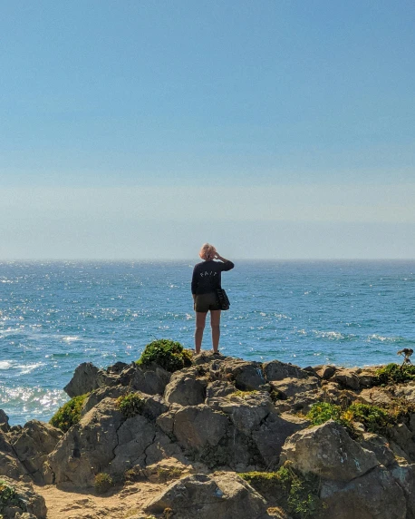 a person looking out over the ocean from the rocky shoreline