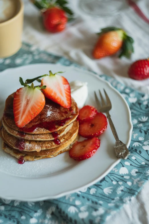 a breakfast plate with a stack of pancakes covered in syrup and strawberries