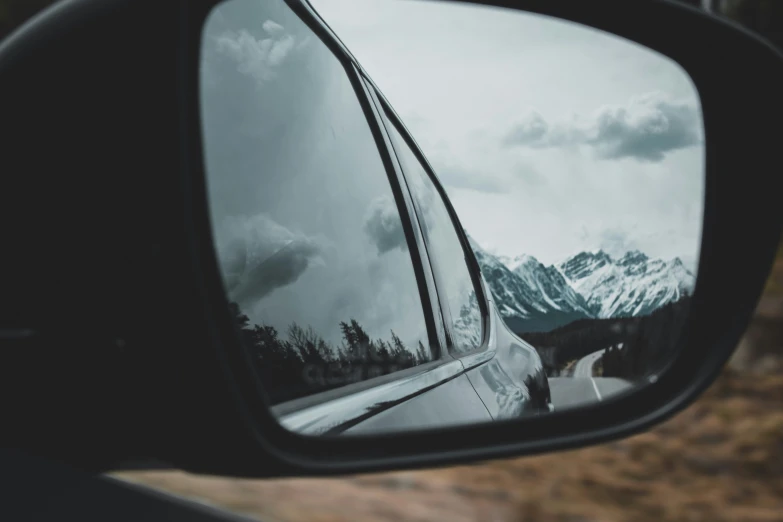 the view from a car's side mirror shows a snowy mountain range