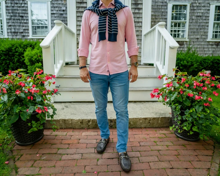 a man wearing a pink shirt and scarf near some flowers