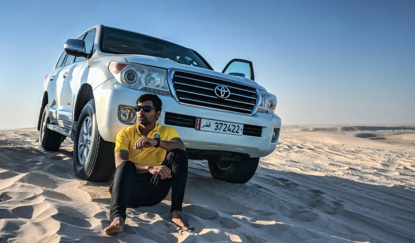 man crouching on sand in front of his suv