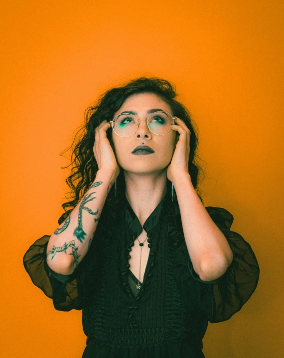 woman with tattoos and holding hands near face against an orange background