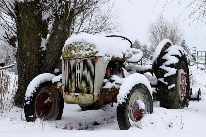 the old tractor is parked in the snow near trees