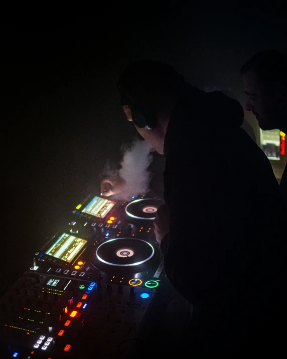 djs are looking at a music device on a dark surface