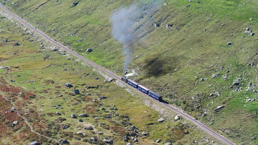 an aerial view of a train in the distance with smoke billowing out the front