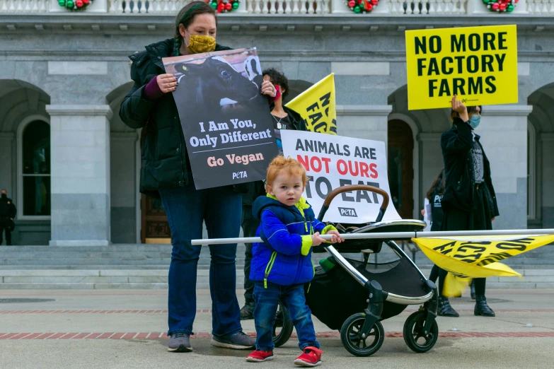 a couple of women holding a sign while a baby stands in a h chair