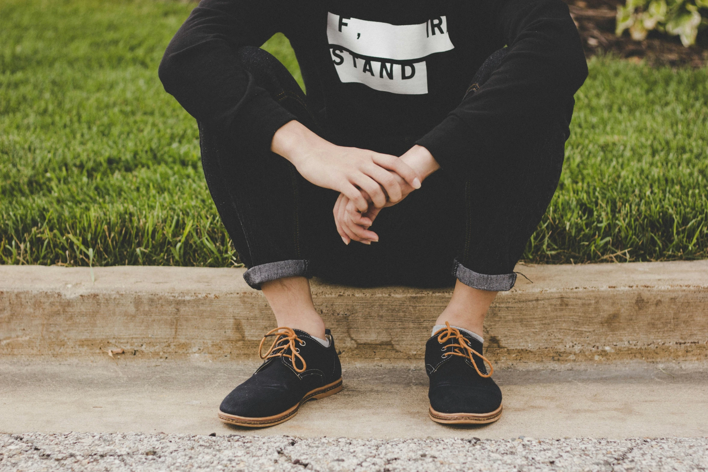 a young man sitting in the grass wearing black shoes