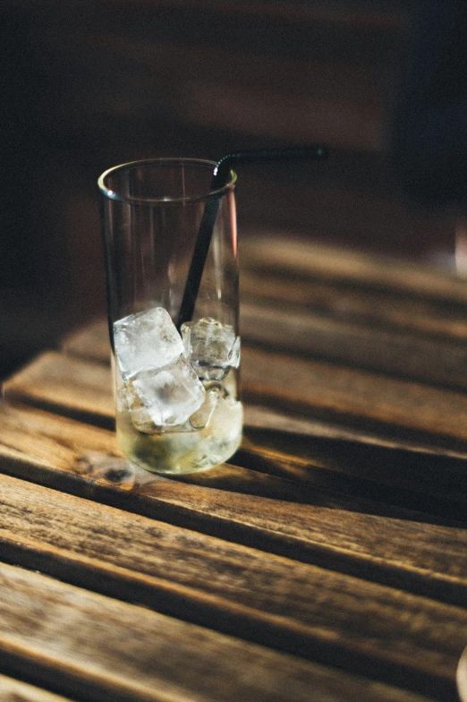 a glass with ice cubes in it on top of a wooden table