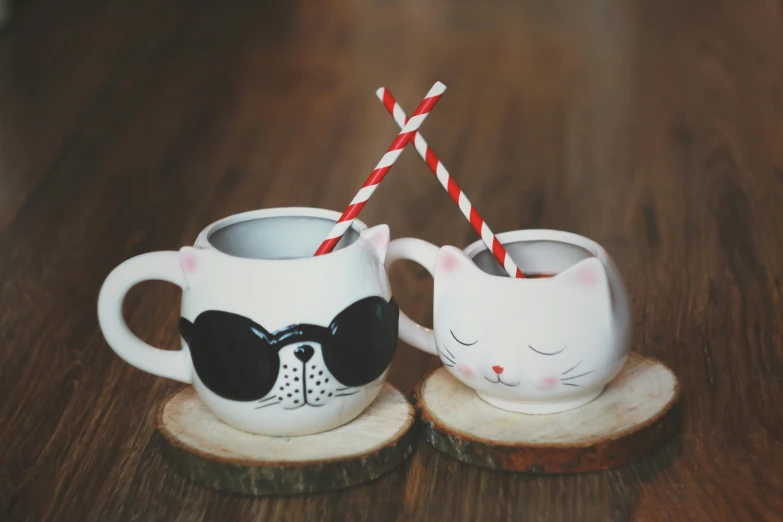 two mugs with cat faces painted on them next to straws