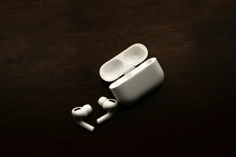 a pair of white ear buds and a black apple wireless headphones on a wooden surface